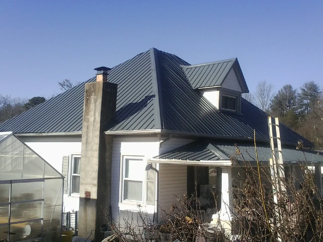 Dark blue standing seam metal roof on a white farmhouse with dormer — Slate & Tile Roof Repair by Roofing Brothers in Golden