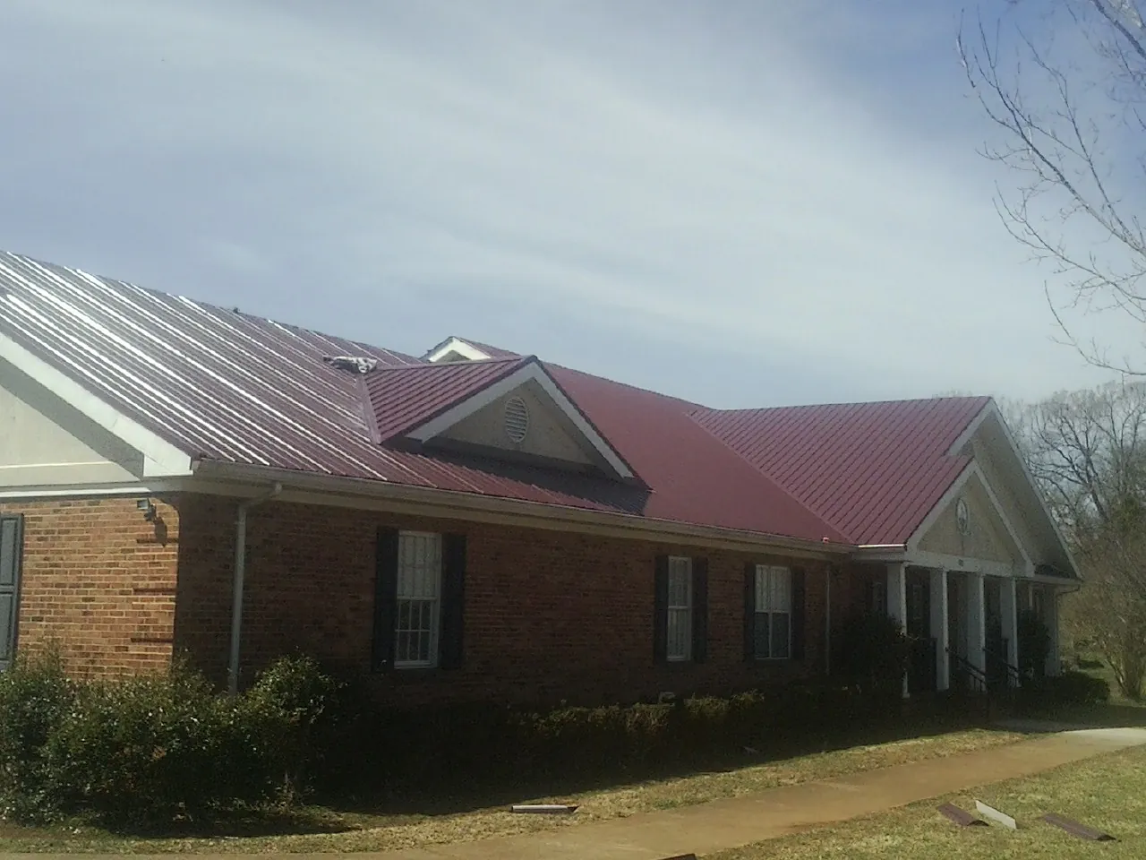 Red metal roof with gabled entries on a long brick building, from a Hail Damage Roof Repair job in Golden