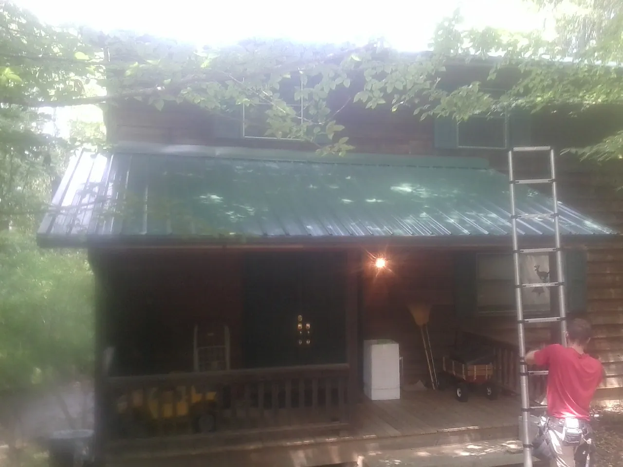 Worker on a ladder at the green porch roof of a wooded cabin in Golden