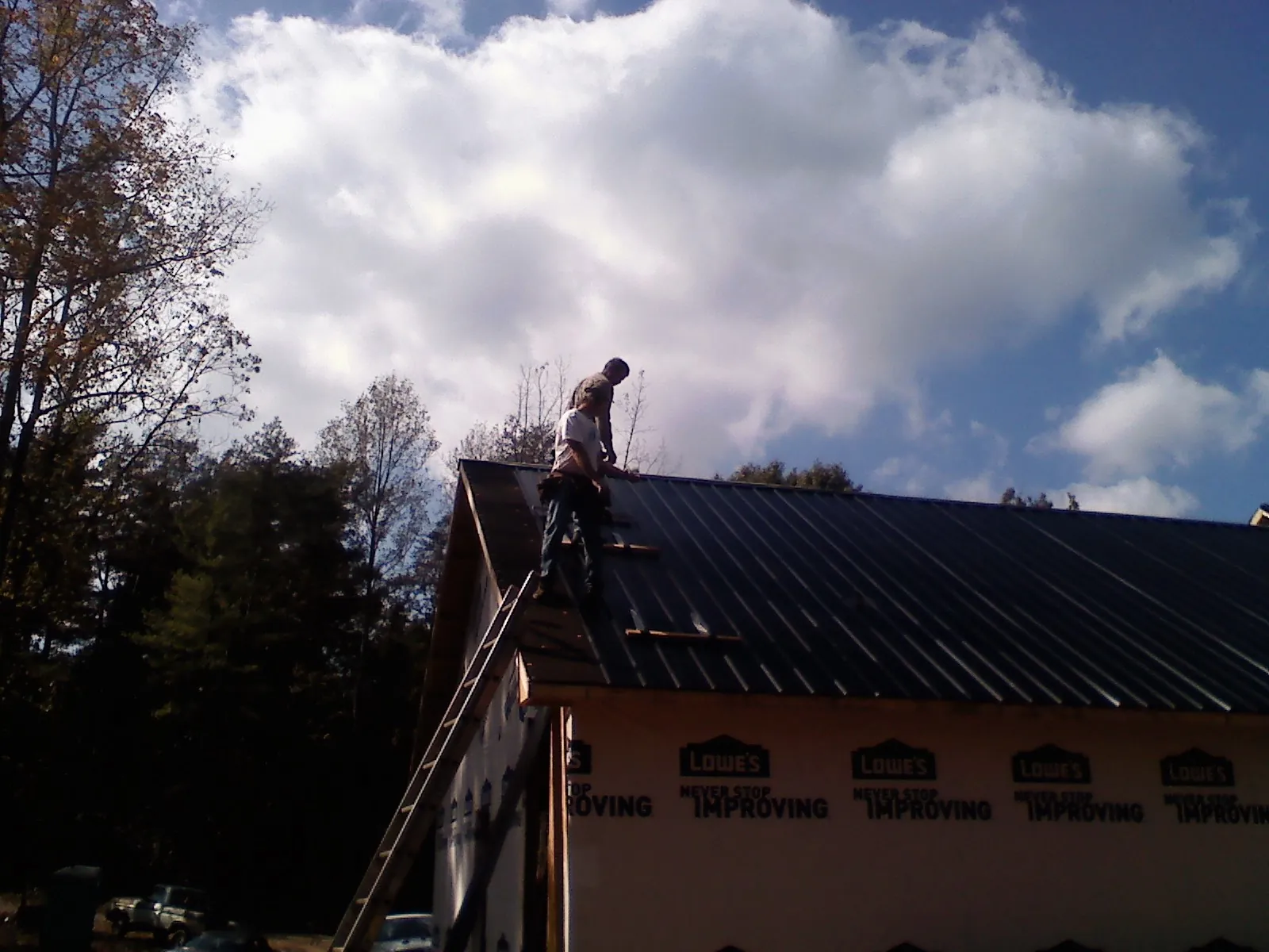 Roofer fastening dark metal panels high against a cloudy sky, from a Roof Inspection job in Golden