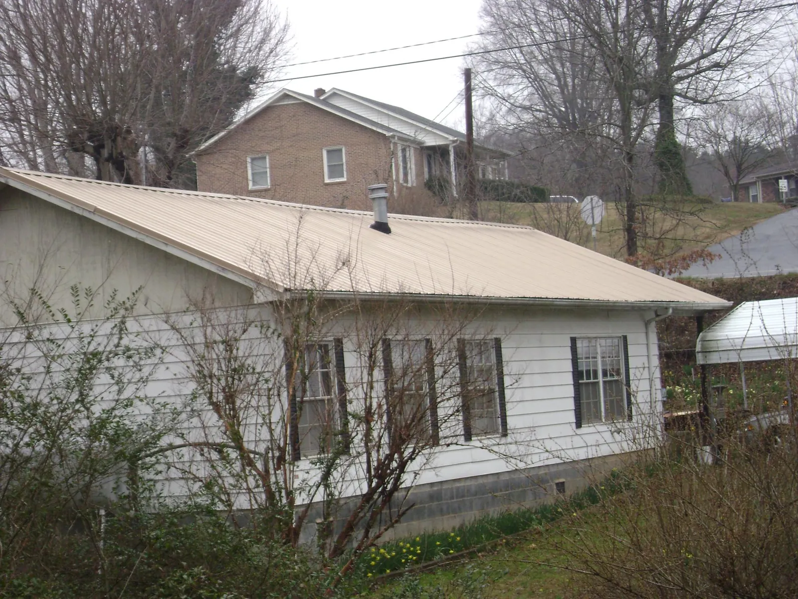Tan metal roof on a white sided house set into a hillside — Commercial Roofing by Roofing Brothers in Golden